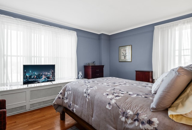 bedroom with ornamental molding, multiple windows, and wood finished floors