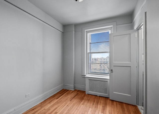 unfurnished room with light wood-style floors, radiator, and baseboards