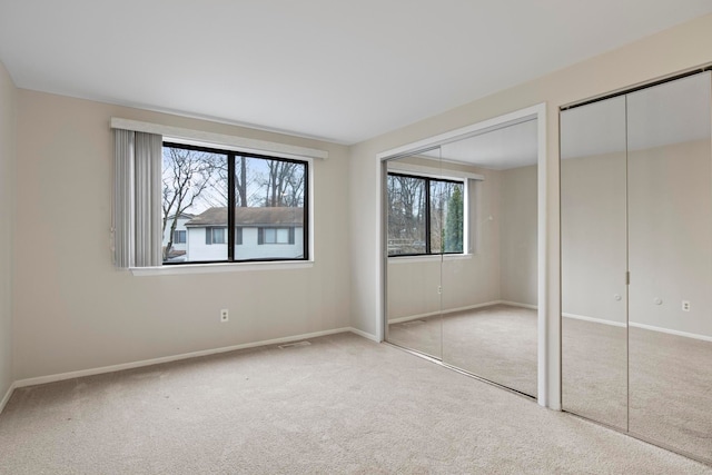 unfurnished bedroom featuring light carpet and two closets