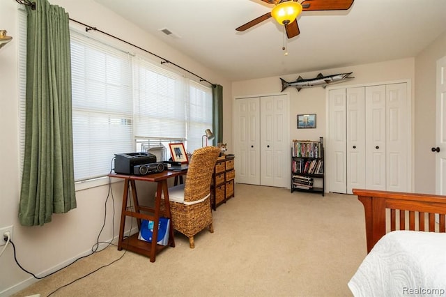 bedroom with light carpet, ceiling fan, and multiple closets