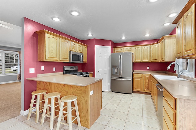 kitchen with sink, appliances with stainless steel finishes, light colored carpet, kitchen peninsula, and a breakfast bar area