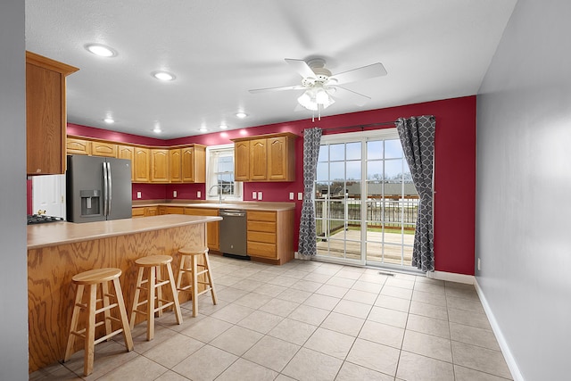 kitchen with a breakfast bar, ceiling fan, light tile patterned floors, appliances with stainless steel finishes, and kitchen peninsula