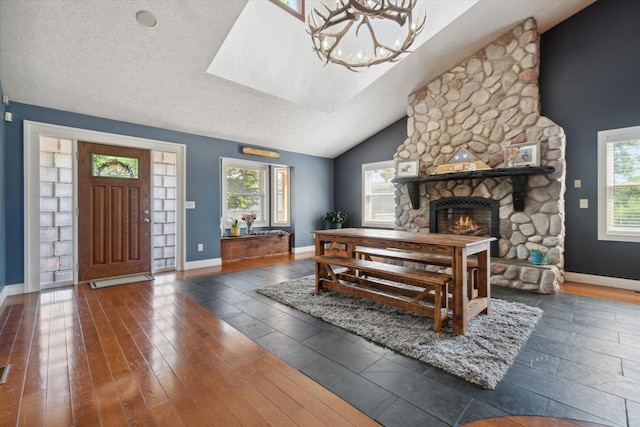 interior space featuring a textured ceiling, vaulted ceiling, dark wood-type flooring, an inviting chandelier, and a stone fireplace