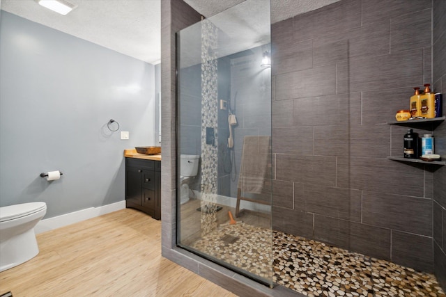 bathroom with a textured ceiling, vanity, tiled shower, wood-type flooring, and toilet