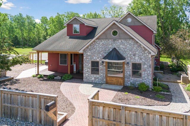 210 E Mcneil St, Corunna, MI 48817 - view of front facade featuring stone siding, a fenced front yard, covered porch, and a shingled roof