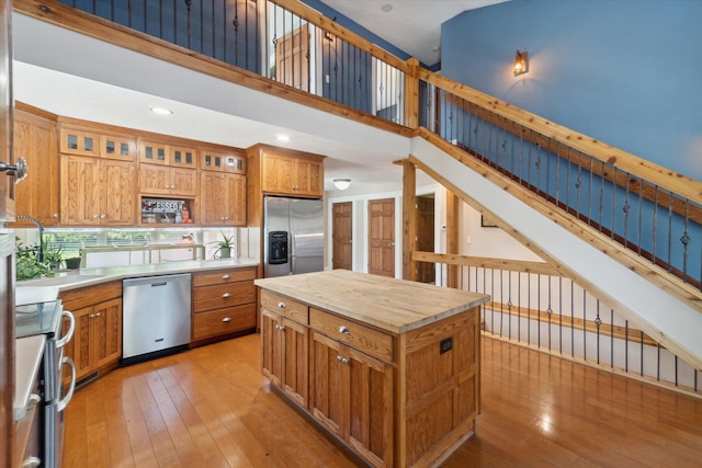 kitchen featuring a towering ceiling, stainless steel appliances, sink, a center island, and light hardwood / wood-style floors