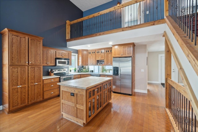 kitchen with appliances with stainless steel finishes, a center island, light hardwood / wood-style floors, and a high ceiling