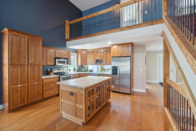 210 E Mcneil St, Corunna, MI 48817 - kitchen featuring appliances with stainless steel finishes, a high ceiling, open shelves, brown cabinetry, and light wood-type flooring