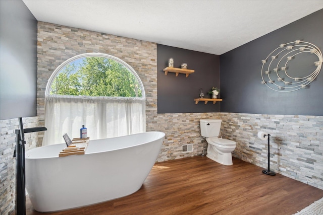 bathroom with a washtub, hardwood / wood-style floors, and toilet