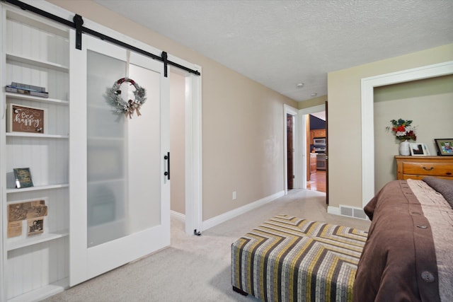 bedroom with a textured ceiling, a barn door, and light carpet