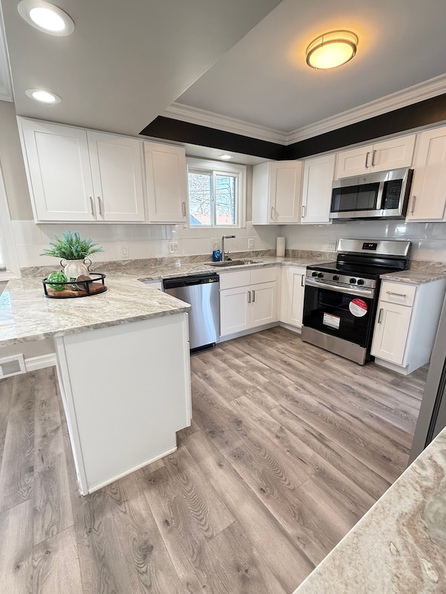 kitchen with stainless steel appliances, light stone counters, kitchen peninsula, light hardwood / wood-style floors, and white cabinets