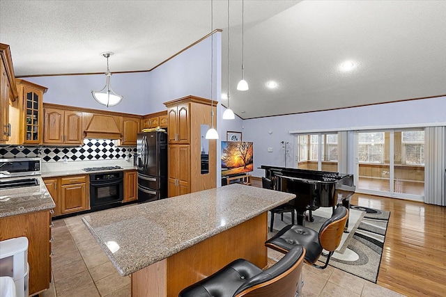 kitchen with black appliances, tasteful backsplash, a kitchen island, light stone counters, and custom range hood