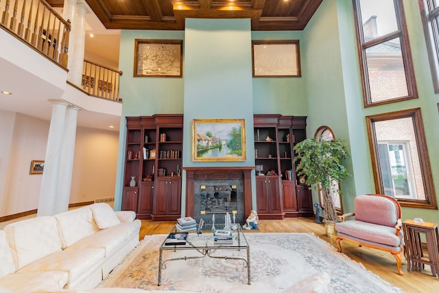 living room with coffered ceiling, light hardwood / wood-style flooring, ornate columns, a towering ceiling, and beamed ceiling