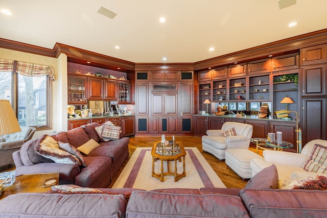 living room featuring bar area, built in shelves, crown molding, and light hardwood / wood-style flooring