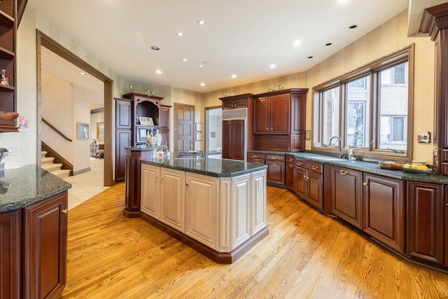 kitchen featuring paneled refrigerator, sink, a center island with sink, dark stone countertops, and light hardwood / wood-style floors