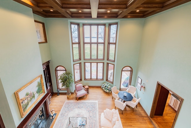 living area featuring coffered ceiling, light hardwood / wood-style flooring, ornamental molding, a towering ceiling, and beamed ceiling