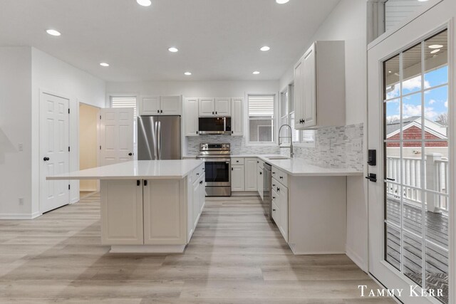 kitchen with appliances with stainless steel finishes, tasteful backsplash, sink, a center island, and white cabinetry