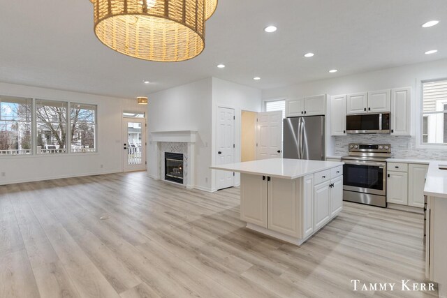 kitchen featuring a center island, a high end fireplace, light hardwood / wood-style floors, white cabinets, and appliances with stainless steel finishes