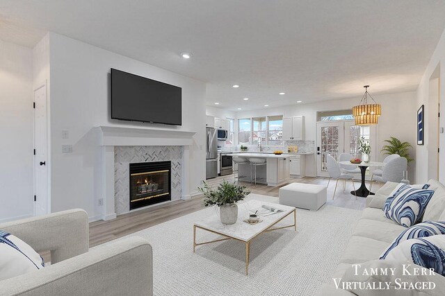 living room featuring a tile fireplace, an inviting chandelier, french doors, sink, and light hardwood / wood-style flooring