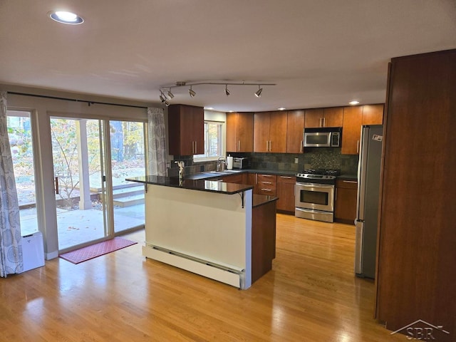 kitchen with kitchen peninsula, appliances with stainless steel finishes, a baseboard heating unit, sink, and light hardwood / wood-style flooring