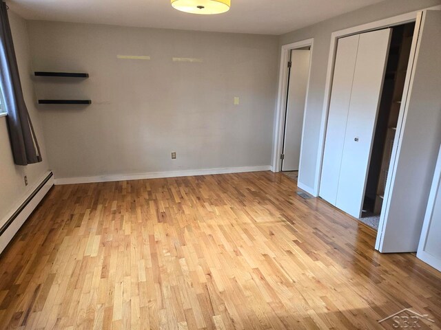 unfurnished bedroom with baseboard heating and light wood-type flooring