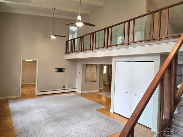 unfurnished living room with baseboard heating, ceiling fan, high vaulted ceiling, beamed ceiling, and hardwood / wood-style floors