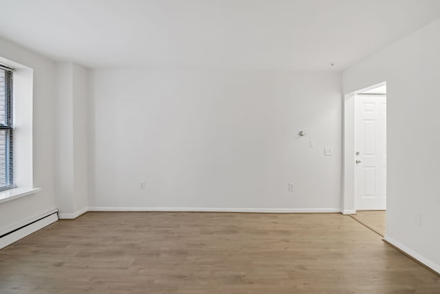 spare room featuring baseboard heating and light hardwood / wood-style flooring