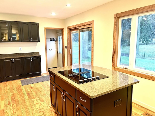 kitchen with black electric cooktop, light stone countertops, light hardwood / wood-style flooring, and dark brown cabinets