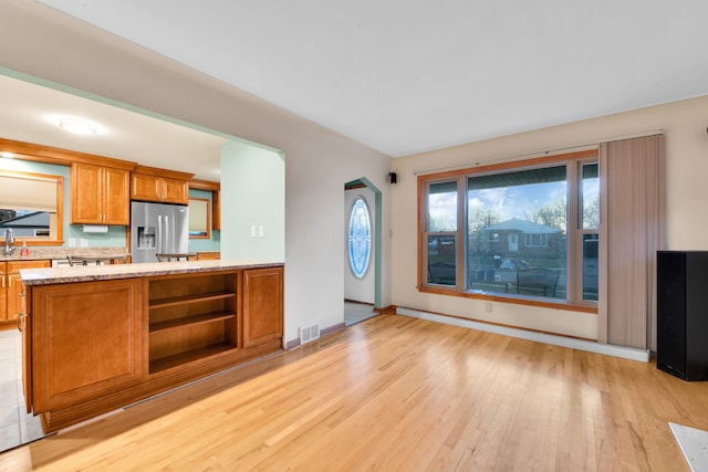 kitchen featuring kitchen peninsula, backsplash, sink, stainless steel fridge with ice dispenser, and light hardwood / wood-style floors