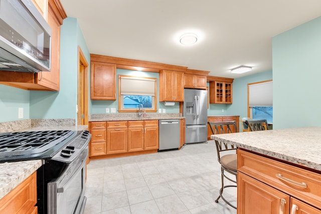 kitchen with light stone counters, sink, a kitchen bar, and stainless steel appliances