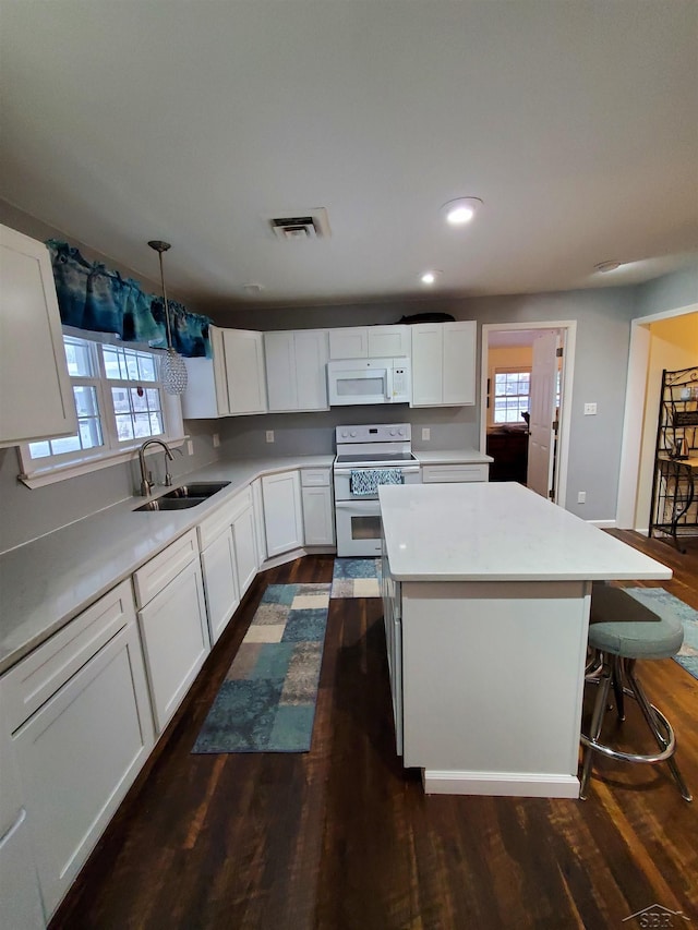 kitchen with a center island, white appliances, sink, hanging light fixtures, and white cabinetry