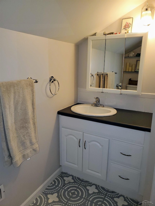 bathroom with vanity, baseboards, vaulted ceiling, and tile patterned floors