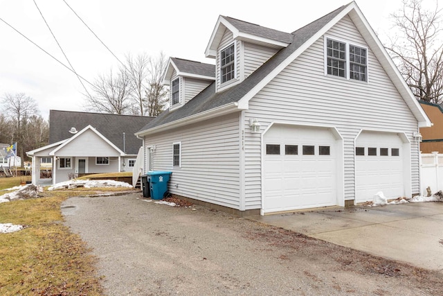 view of side of property featuring a garage, roof with shingles, and driveway