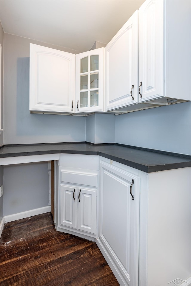 kitchen with white cabinetry, dark countertops, dark wood-style floors, and built in desk