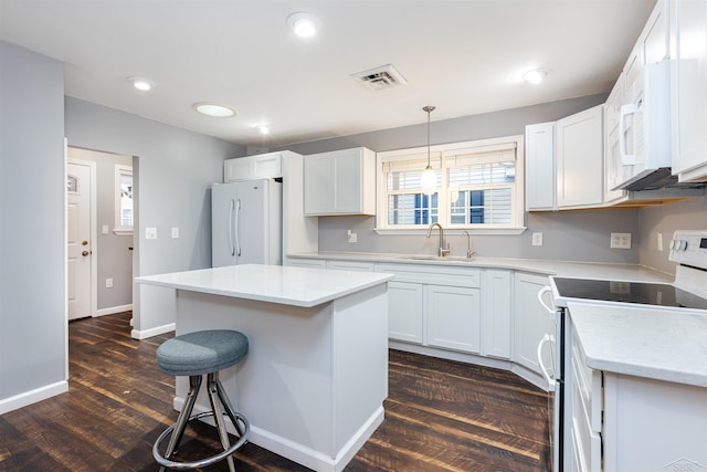 kitchen featuring visible vents, a kitchen breakfast bar, dark wood-style floors, white appliances, and a sink