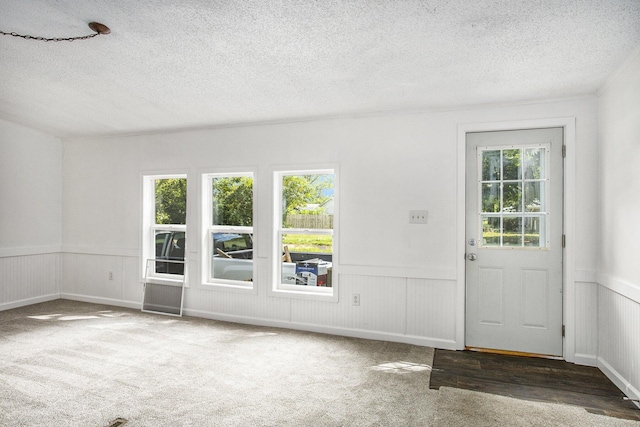 entryway with dark colored carpet, a textured ceiling, and plenty of natural light