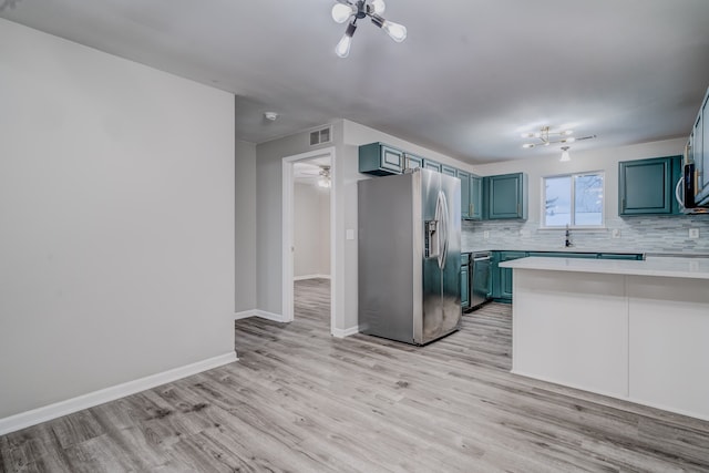 kitchen with kitchen peninsula, tasteful backsplash, stainless steel appliances, blue cabinetry, and light hardwood / wood-style floors