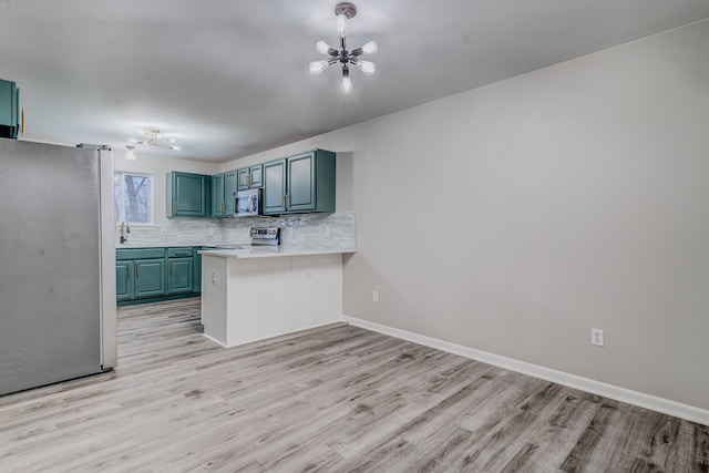 kitchen featuring kitchen peninsula, light wood-type flooring, tasteful backsplash, stainless steel appliances, and an inviting chandelier