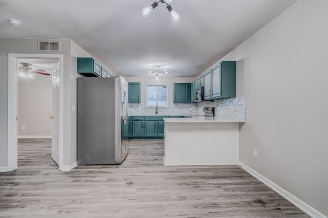 kitchen with kitchen peninsula, light hardwood / wood-style flooring, appliances with stainless steel finishes, and tasteful backsplash