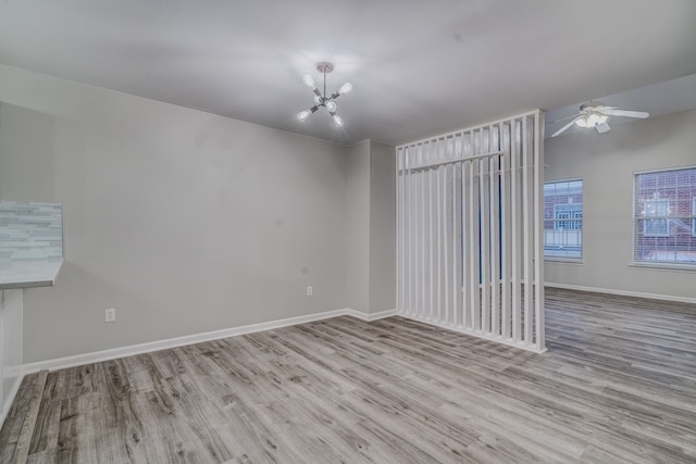 unfurnished room with ceiling fan with notable chandelier and light wood-type flooring