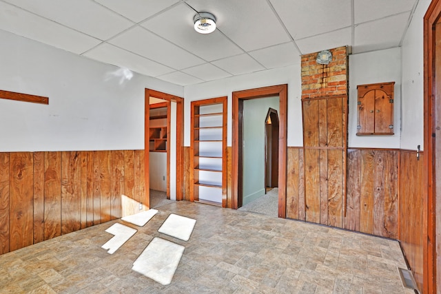 unfurnished room featuring a paneled ceiling and wood walls