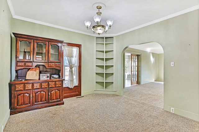 interior space with carpet flooring, built in shelves, an inviting chandelier, and crown molding