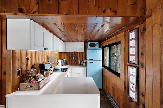 kitchen with white cabinets, refrigerator, wooden ceiling, and wood walls