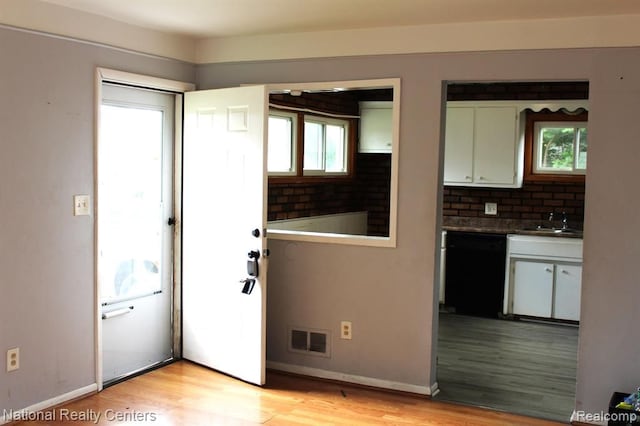 kitchen featuring light wood-type flooring, backsplash, sink, dishwasher, and white cabinetry