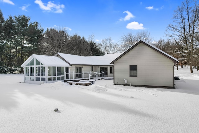 snow covered rear of property with a deck and a sunroom