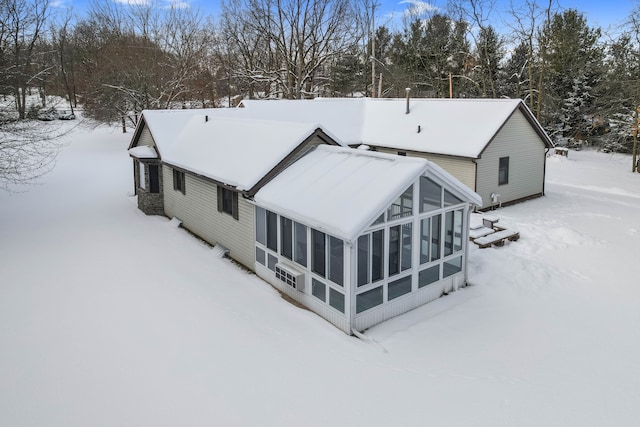 snow covered back of property featuring a sunroom