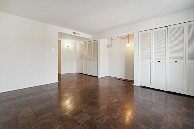 unfurnished bedroom featuring multiple closets and dark parquet flooring