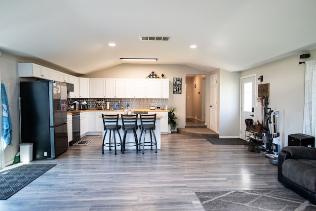 kitchen with a breakfast bar, black appliances, vaulted ceiling, tasteful backsplash, and white cabinetry