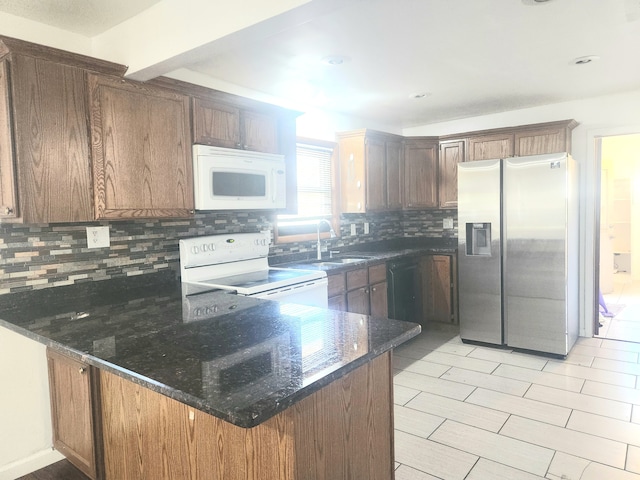 kitchen with tasteful backsplash, kitchen peninsula, dark stone counters, and white appliances