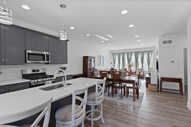 kitchen featuring sink, tasteful backsplash, pendant lighting, appliances with stainless steel finishes, and light wood-type flooring